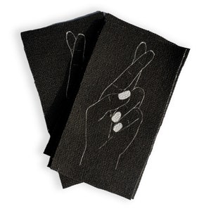 May include: Two black fabric patches with white embroidered outlines of crossed fingers. The patches are folded together.