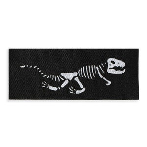 May include: A black fabric patch with a white silhouette of a dinosaur skeleton running. The dinosaur is facing right and has a long tail.