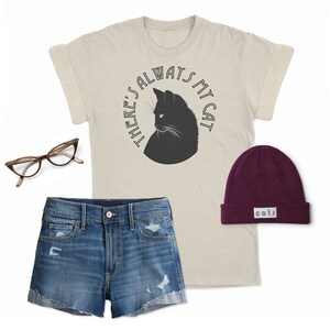 May include: A beige t-shirt with a black cat silhouette and the text "There's always my cat" in a circle. The shirt is paired with denim shorts and a burgundy beanie with the word "cats" on it.