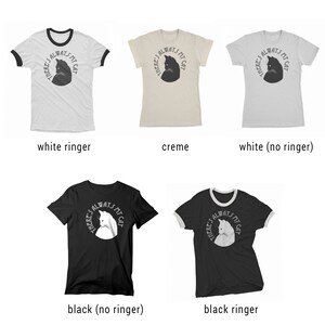 May include: Five t-shirts in different colors and styles featuring a black and white graphic of a cat's head with the text "THERE'S ALWAYS MY CAT". The t-shirts are available in white with a black ringer, creme, white without a ringer, black without a ringer, and black with a white ringer.
