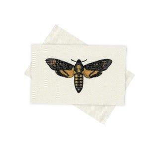 May include: A white fabric patch with a black and yellow moth embroidered on it. The moth has a wingspan of about 2 inches.