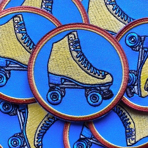 May include: Close-up of several yellow and blue embroidered roller skate patches. The patches are circular and have a red and gold border. The roller skates are on a blue background.