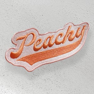 May include: Peachy embroidered iron-on patch in a pink and orange color scheme. The patch is shaped like a curved banner with the word "Peachy" in a cursive font.