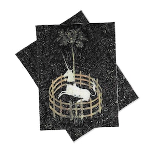 May include: Two black fabric patches with a white unicorn in a circular fence with a tree behind it. The unicorn is facing the right side of the image. The background is black with a speckled pattern.
