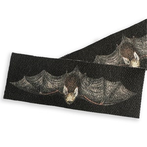 May include: Black fabric ribbon with a repeating pattern of bats flying in front of a dark background. The bats are depicted in a realistic style with detailed wings and faces.