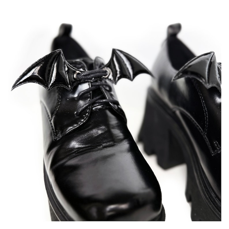 K&ouml;nnte beinhalten: Schwarze Plateauschuhe aus Leder mit Fledermausfl&uuml;gel-Schnallen. Die Schuhe haben einen Schn&uuml;rverschluss und eine dicke Plateau-Sohle.