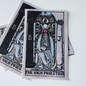 May include: Several fabric patches featuring the High Priestess tarot card design. The illustration is in black, white, and pale blue, with the text "THE HIGH PRIESTESS" at the bottom. The patches have a woven texture.