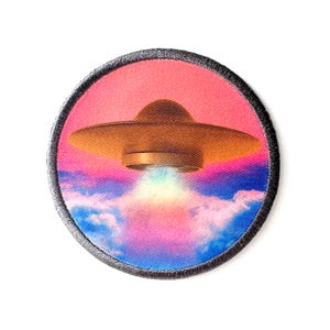 May include: A round, black-edged patch with a colorful image of a flying saucer emerging from pink and blue clouds.