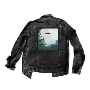 May include: A black denim jacket with a patch on the back. The patch features a photo of a flying saucer over a forest.