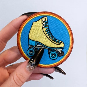 May include: A yellow and blue embroidered iron-on patch of a roller skate with wheels. The patch is circular and has a blue background with an orange border.