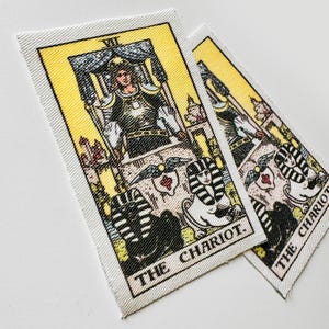May include: Two rectangular fabric patches featuring the Chariot tarot card. The cards have a yellow background with a detailed illustration of a figure in armor, a chariot, and sphinxes. The text "THE CHARIOT" is printed at the bottom.