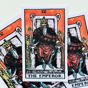 May include: A rectangular fabric patch featuring the Emperor tarot card illustration. The design shows a bearded figure in a crown and red robes sitting on a stone throne with ram heads. The Roman numeral IV and the text THE EMPEROR are visible.