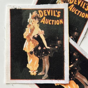 May include: A vintage-style fabric patch featuring a woman in a black dress with a floral pattern and a man in a yellow costume. The text "DEVIL'S AUCTION" is printed in yellow on a black background.