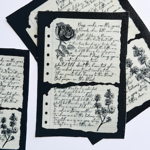 May include: A rectangular fabric patch with a black border featuring two cream-colored paper-like sections printed with black cursive text and botanical illustrations of a rose and small flowers, resembling torn notebook pages.