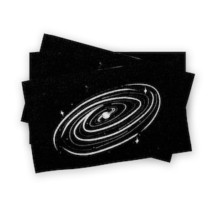 May include: Black rectangular cards with a white galaxy illustration. The galaxy design features concentric spiral lines with a central ring and surrounding stars. The cards are stacked, creating a layered effect.