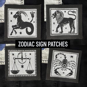 May include: Four black and white iron-on patches featuring zodiac signs. The signs are Capricorn, Leo, Libra, and Scorpio. The patches are on a black background with white stitching around the edges.