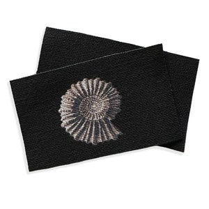 May include: A black fabric label with a white and gray ammonite fossil design.