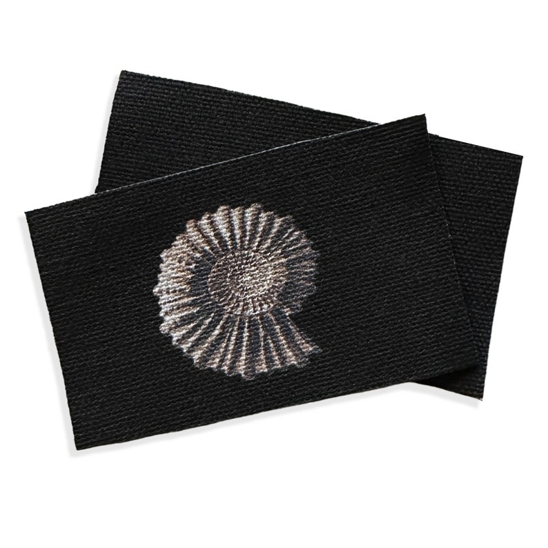 May include: A black fabric label with a white and gray ammonite fossil design.