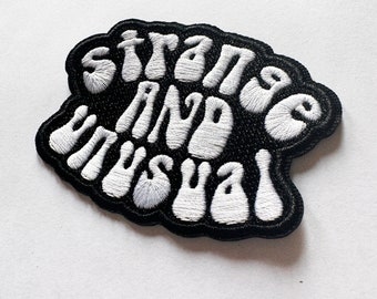 May include: Black embroidered patch with white lettering that reads "Strange and Unusual".