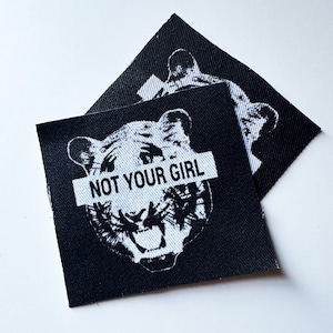 May include: Black and white iron-on patch with a tiger face and the text "NOT YOUR GIRL" across the eyes.