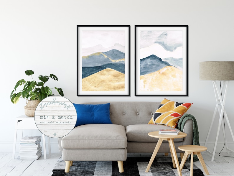 May include: Two framed watercolour mountain prints in black frames. The artwork features blue and gold hues. The image includes the text "Starchhouse" and "Mix & Match each sold separately". The prints are displayed above a grey sofa.
