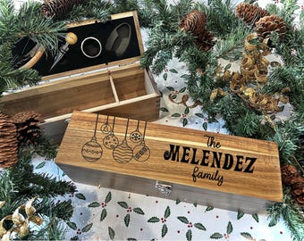 Könnte beinhalten: Holzkiste mit einem Scharnierdeckel, graviert mit Weihnachtskugeln und dem Text "The Melendez family". Die Kiste ist geöffnet und zeigt ein schwarzes Samtinnere mit einem Flaschenöffner, einem Korkenzieher und einem Flaschenverschluss.