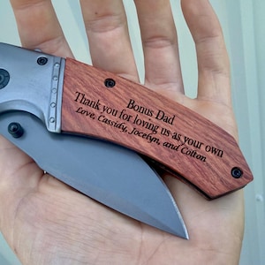 May include: A folding pocket knife with a silver blade and a wooden handle. The handle is engraved with the text "Bonus Dad, Thank you for loving us as your own, Love, Cassidy, Jocelyn, and Colton."