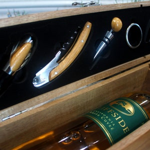 K&ouml;nnte beinhalten: Eine Holzkiste mit einer Flasche Wein und einem Weinkorkenzieher-Set. Die Kiste ist ge&ouml;ffnet und das Weinkorkenzieher-Set ist sichtbar. Die Weinflasche ist mit "Cliffside California White Cuvee" beschriftet.