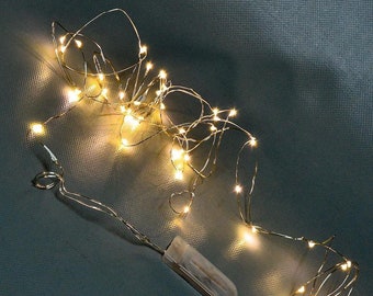 May include: A string of warm white LED fairy lights with a battery pack. The lights are wrapped around each other and are on a silver wire.