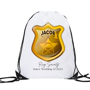 May include: White drawstring bag with a gold badge featuring a star and the text "JACOB" and the text "Ring Security Baker Wedding 9.7.2024".