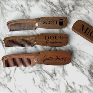 May include: Four wooden pocket combs with personalized engravings. The combs are brown and have a black engraved design. The names on the combs are Scott, Doug, Mig, and Justin Henry.