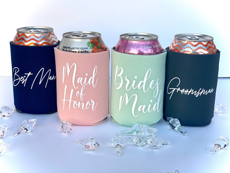 May include: Four beverage insulators with different colors and text. The insulators are navy blue, pink, light green, and black. The text on the insulators reads "Best Man", "Maid of Honor", "Bridesmaid", and "Groomsman".