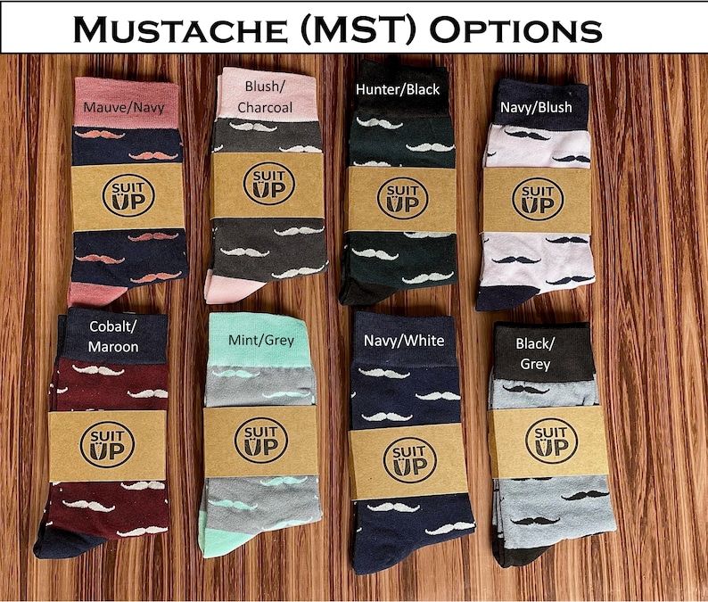 May include: A collection of eight pairs of socks with mustache patterns in various color combinations, including mauve/navy, blush/charcoal, hunter/black, and navy/blush. Each pair is wrapped with a brown paper band that reads "SUIT UP". The text "MUSTACHE (MST) OPTIONS" is at the top.