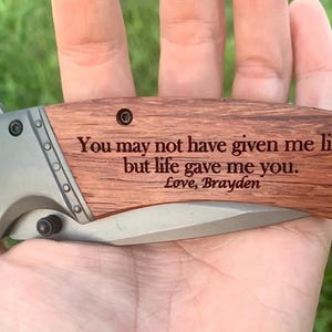 May include: A folding pocket knife with a wooden handle and a silver blade. The wooden handle is engraved with the text "You may not have given me life, but life gave me you. Love, Brayden."