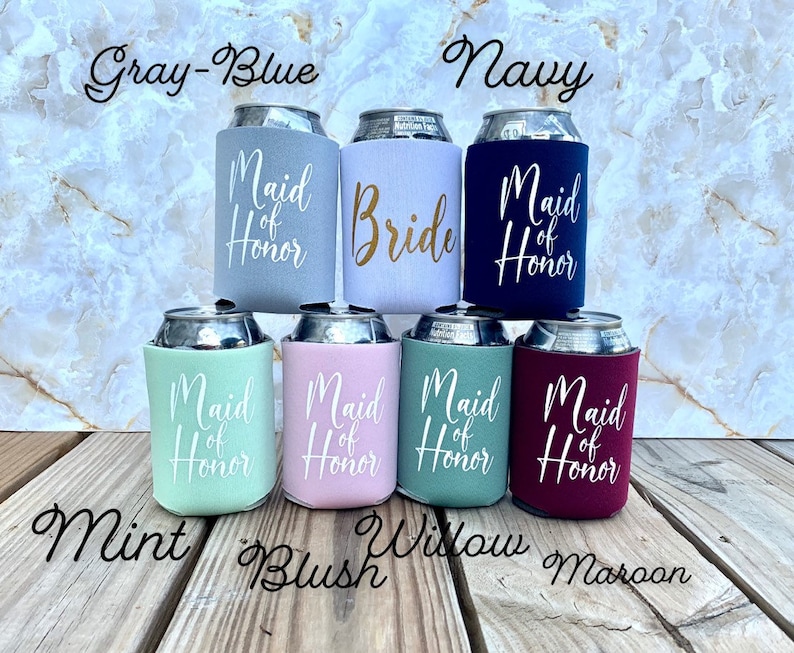May include: Set of seven beverage insulators with different colors and text. The colors are gray-blue, navy, mint, blush, willow, and maroon. The text on the insulators reads "Maid of Honor" and "Bride".
