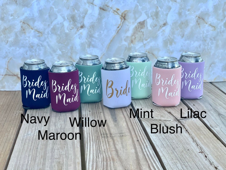 May include: Six different colored can coolers with the text "Brides Maid" or "Bride" printed in white. The colors are navy, maroon, green, white, pink, and lilac.