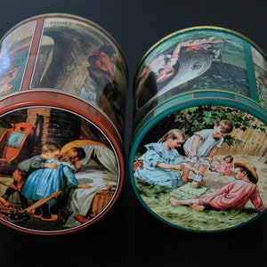 Puede incluir: Dos latas de metal vintage con ilustraciones coloridas. Una lata tiene un borde rojo y representa a niños en una habitación. La otra lata tiene un borde verde y muestra a niños jugando al aire libre. Ambas latas son cilíndricas.