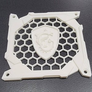 May include: A white computer component with a honeycomb pattern and a central emblem featuring a dragon. The component has a rectangular frame with mounting holes and a textured surface.
