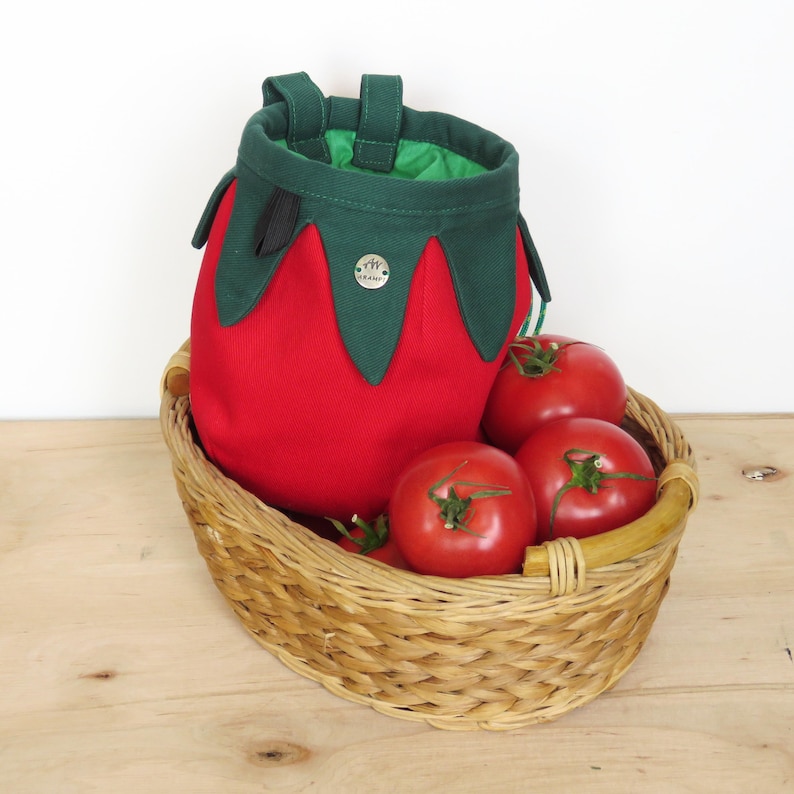 red tomato shape with dark green leaves chalk bag for climbing in rock and gym, with real tomatoes in basket