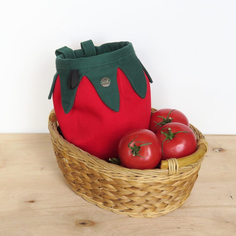 red tomato shape with dark green leaves chalk bag for climbing in rock and gym, with real tomatoes in basket