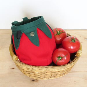 red tomato shape with dark green leaves chalk bag for climbing in rock and gym, with real tomatoes in basket