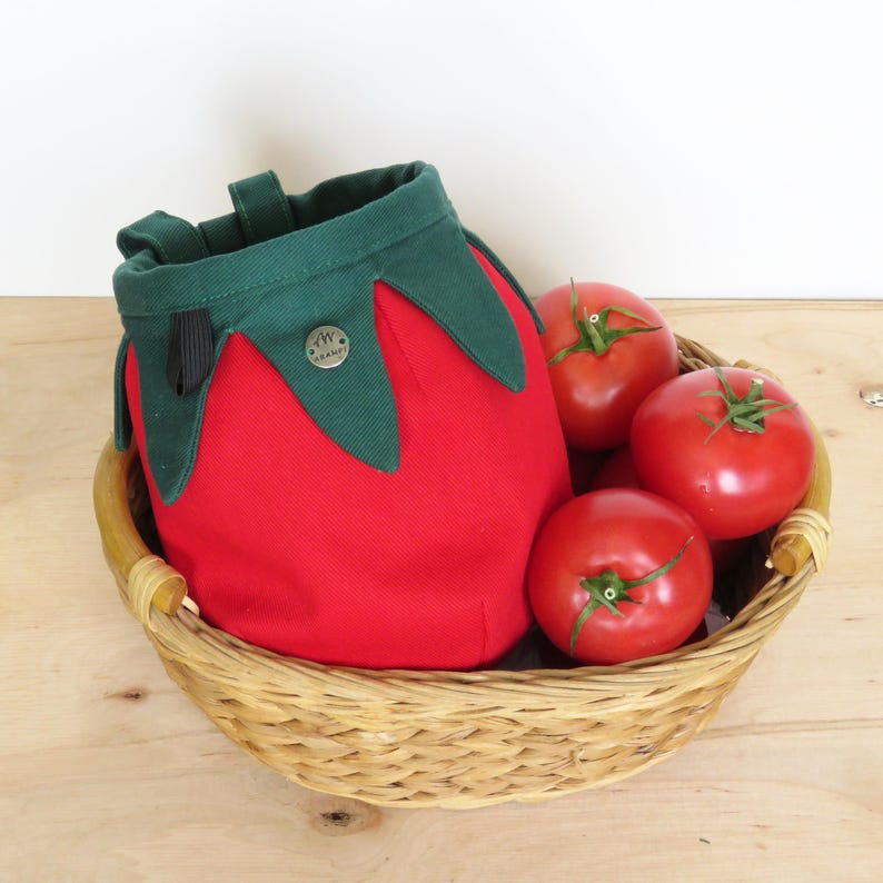 red tomato shape with dark green leaves chalk bag for climbing in rock and gym, with real tomatoes in basket