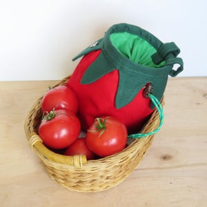 red tomato shape with dark green leaves chalk bag for climbing in rock and gym, with real tomatoes in basket