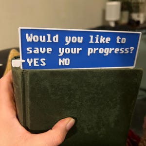 Può includere: Un segnalibro blu con il testo "Would you like to save your progress? YES NO" su di esso.