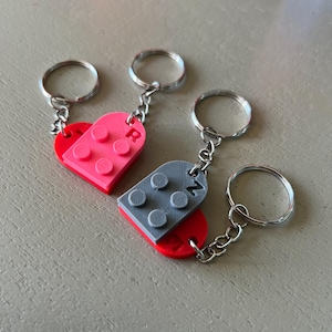 May include: Three keychains with heart-shaped charms. Two keychains feature a red and pink heart design, while the third has a gray and red heart design. Each keychain has a silver ring and chain.