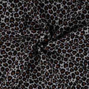 Könnte beinhalten: Nahaufnahme eines Stoffes mit Leopardenmuster. Der Stoff hat einen weißen Hintergrund mit schwarzen und braunen Flecken. Der Stoff ist gefaltet und drapiert, wodurch die Textur und das Muster sichtbar werden.