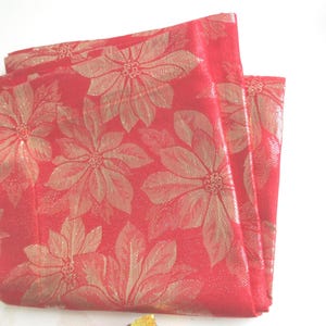 Könnte beinhalten: Gefalteter roter Stoff mit goldenem Blumenmuster. Der Stoff weist ein sich wiederholendes Design aus großen Weihnachtssternen auf. Das Material hat einen leichten Glanz, was darauf hindeutet, dass es für Weihnachtsdekorationen oder Tischdecken verwendet werden kann.