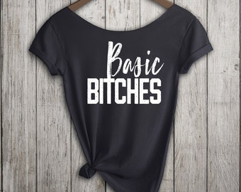Op de afbeelding: Zwart T-shirt met een witte afbeelding met de tekst "Basic Bitches" in een verweerd lettertype.