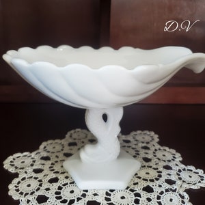 May include: A white, pedestal-style serving bowl with a scalloped rim. The bowl is supported by a stylized, swirling base. The base sits on a hexagonal platform. The initials "D.V" are in the upper right corner.