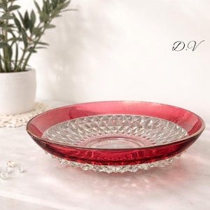 May include: A ruby red glass serving dish with a clear, diamond-patterned center. The rim is a vibrant red, and the base has a textured, scalloped design. The dish is likely used for serving food or as a decorative piece.